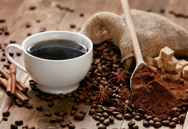 Cup Of Coffee And Coffee Beans On Table. Close Up Of Aromatic Hot Drink With Different Types Of Spices And Coffee On Wooden Table. High Quality Image.